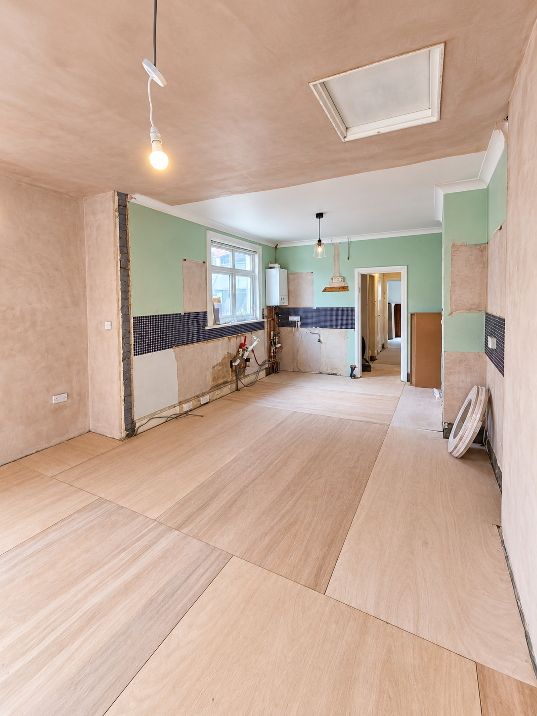 Renovated room showing wall-mounted boiler, exposed plumbing and underfloor heating preparation.