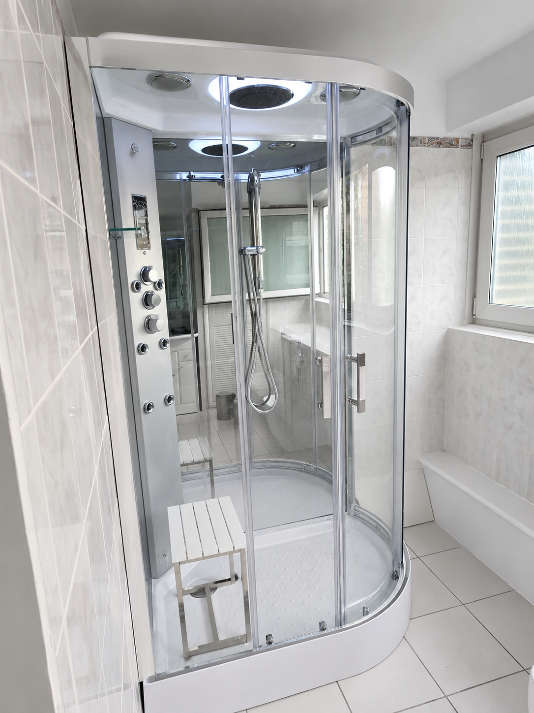 Completed shower cabin with curved glass doors, built-in seat, overhead shower and multiple controls.