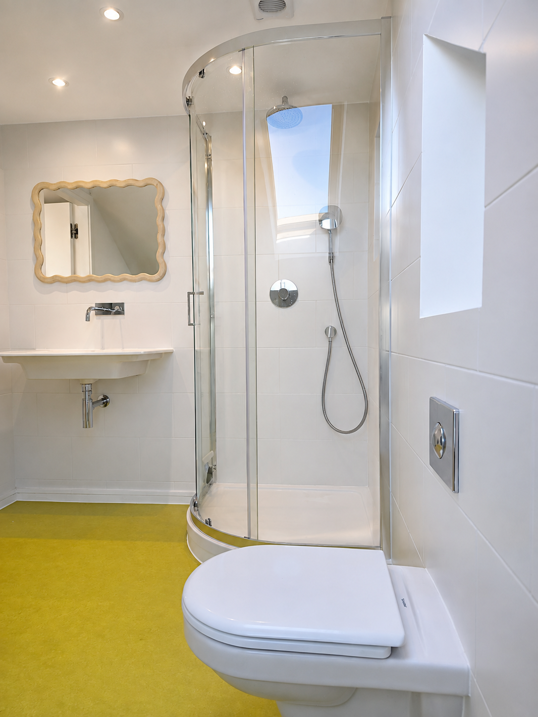 Curved glass shower enclosure beside a wall-mounted basin and wall-hung WC in a tiled