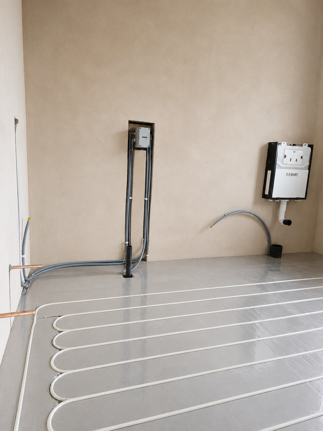 Close view of underfloor heating pipework, copper pipework, conduits and concealed WC plumbing.