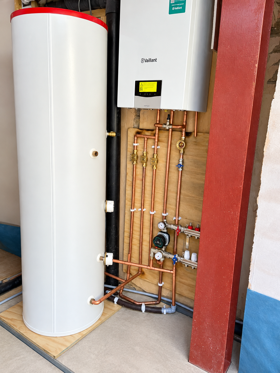 Plumber working on copper pipework beside a large hot water cylinder during a heating installation.