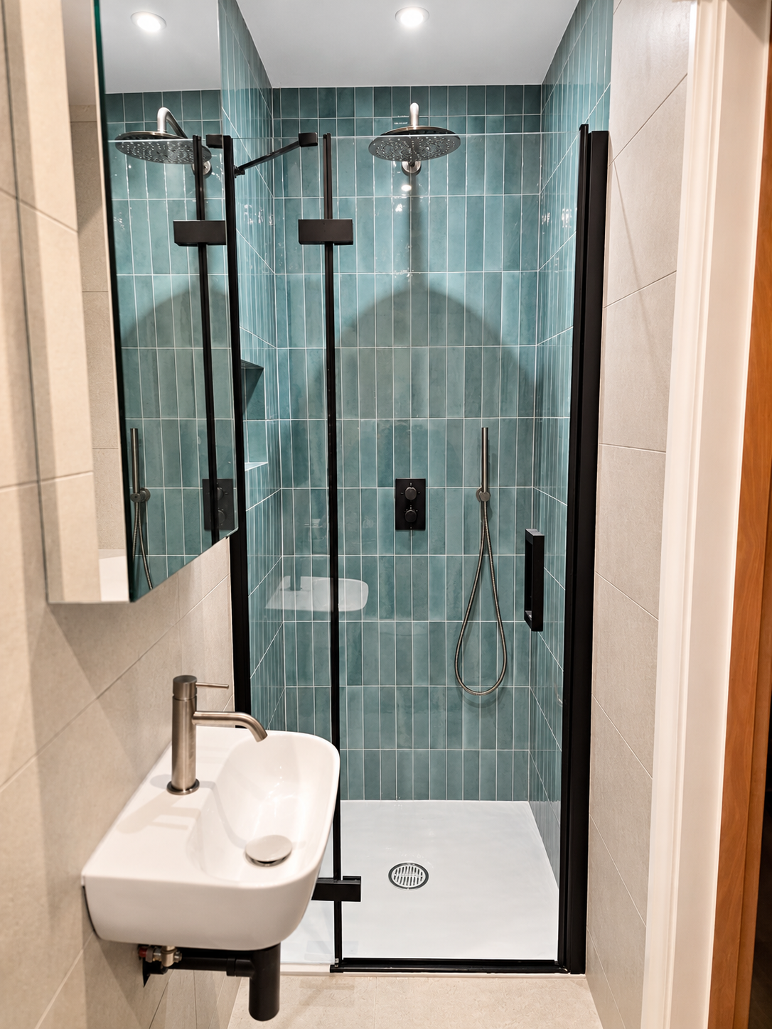 Modern walk-in shower with teal wall tiles, black-framed glass enclosure, rainfall showerhead and white shower tray.
