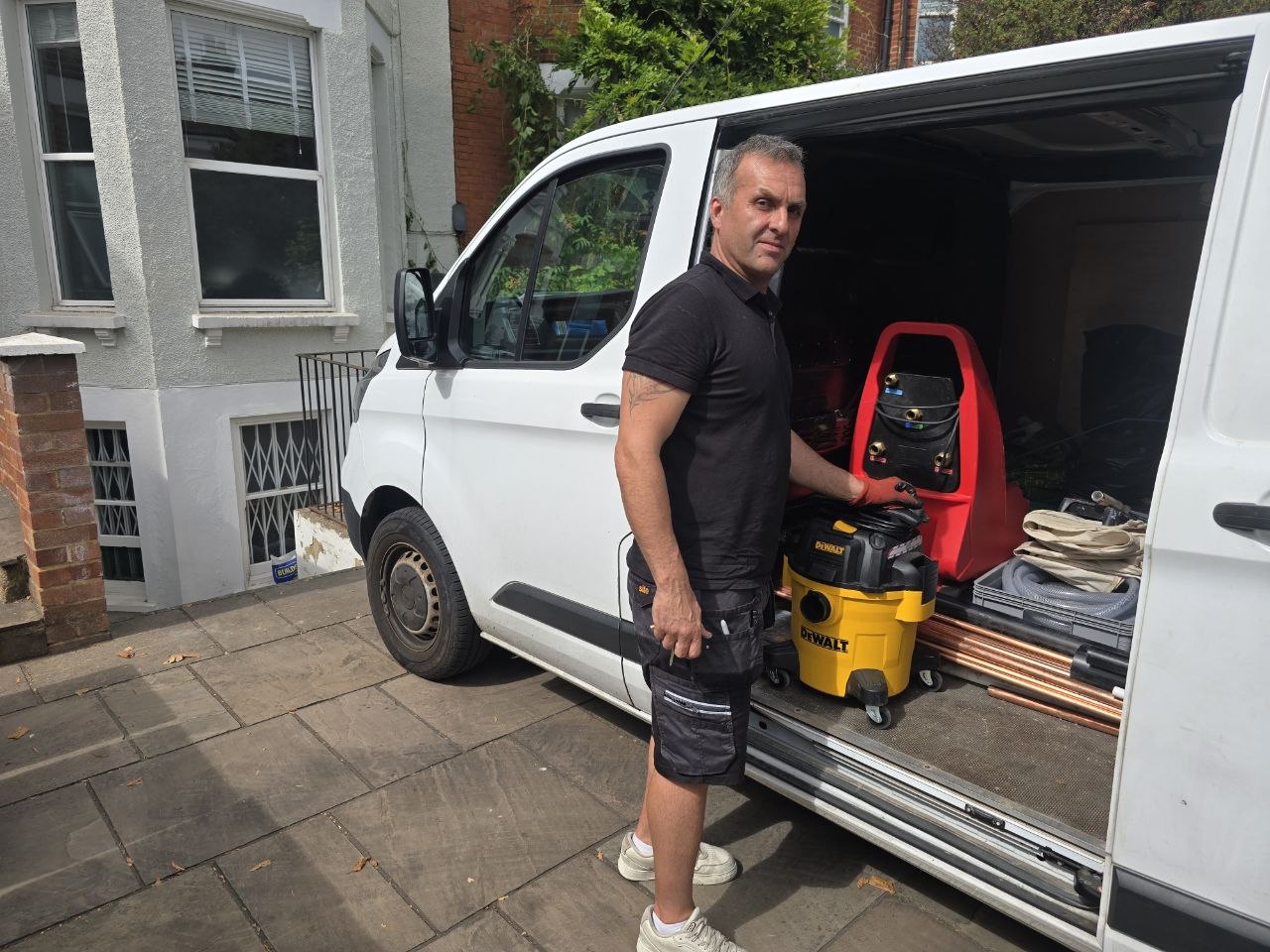 Plumbing and heating engineer with his service van and equipment outside a North London property.