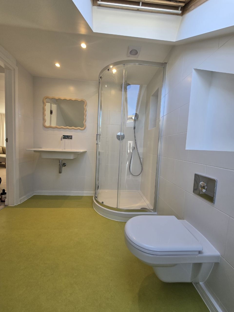 Bathroom with curved shower enclosure, wall-hung WC, wall-mounted basin and skylight.