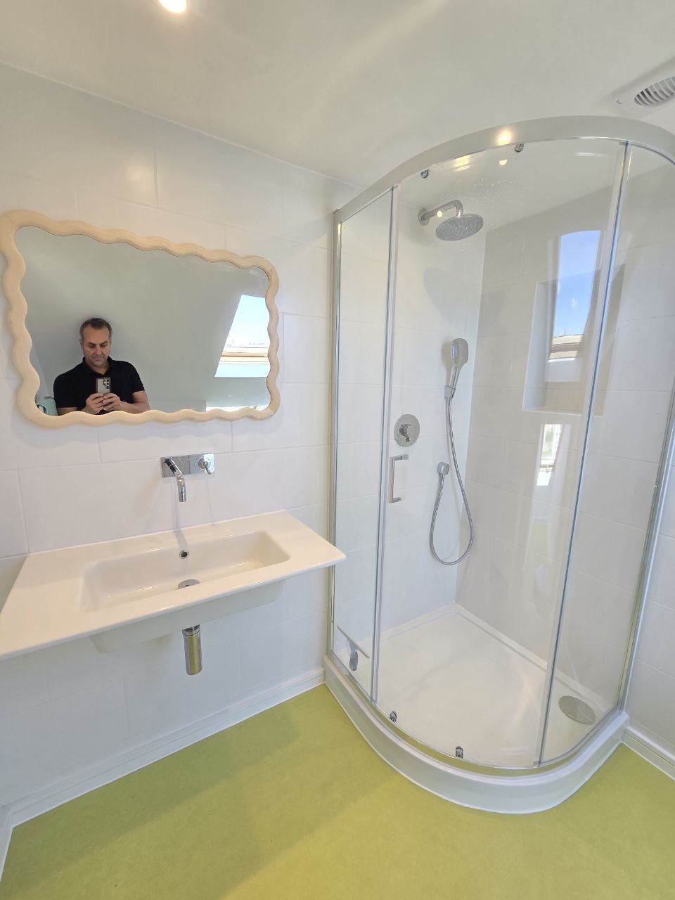 White tiled bathroom with curved glass shower, wall-mounted basin and chrome shower fittings.