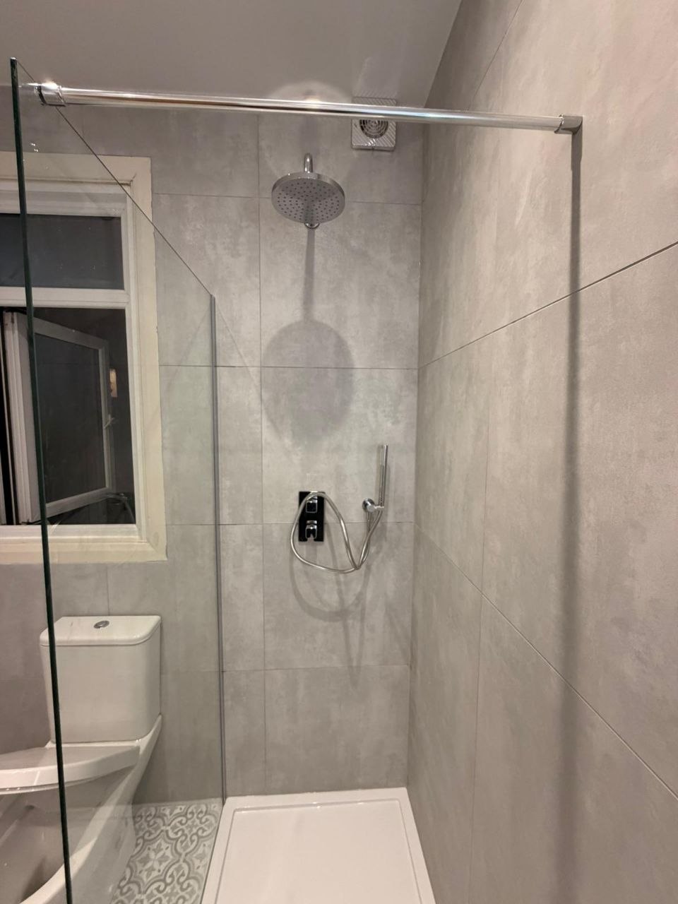 Walk-in shower with rainfall shower head, handheld shower and clear glass screen.