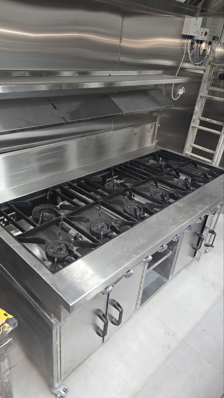 : Stainless-steel commercial cooking range with multiple gas burners and connected kitchen services.