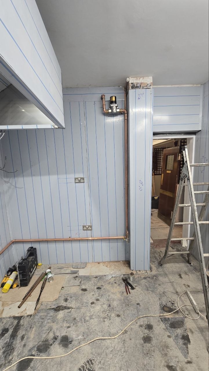 Vertical copper gas pipework and gas control equipment installed beside a commercial kitchen doorway.