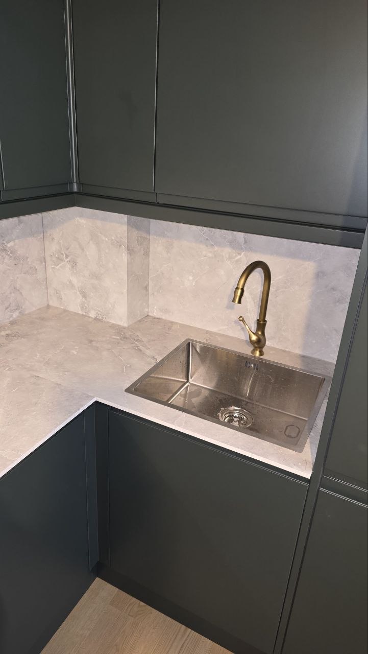 : New stainless-steel kitchen sink with brass-effect tap and light worktop beneath dark cabinets.