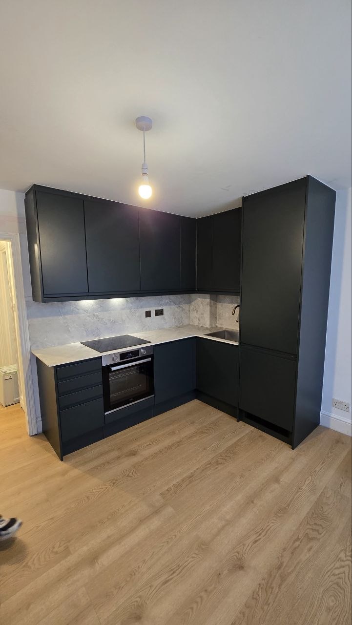 Completed kitchen with dark fitted cabinets, light worktops, integrated oven and wood-effect flooring.