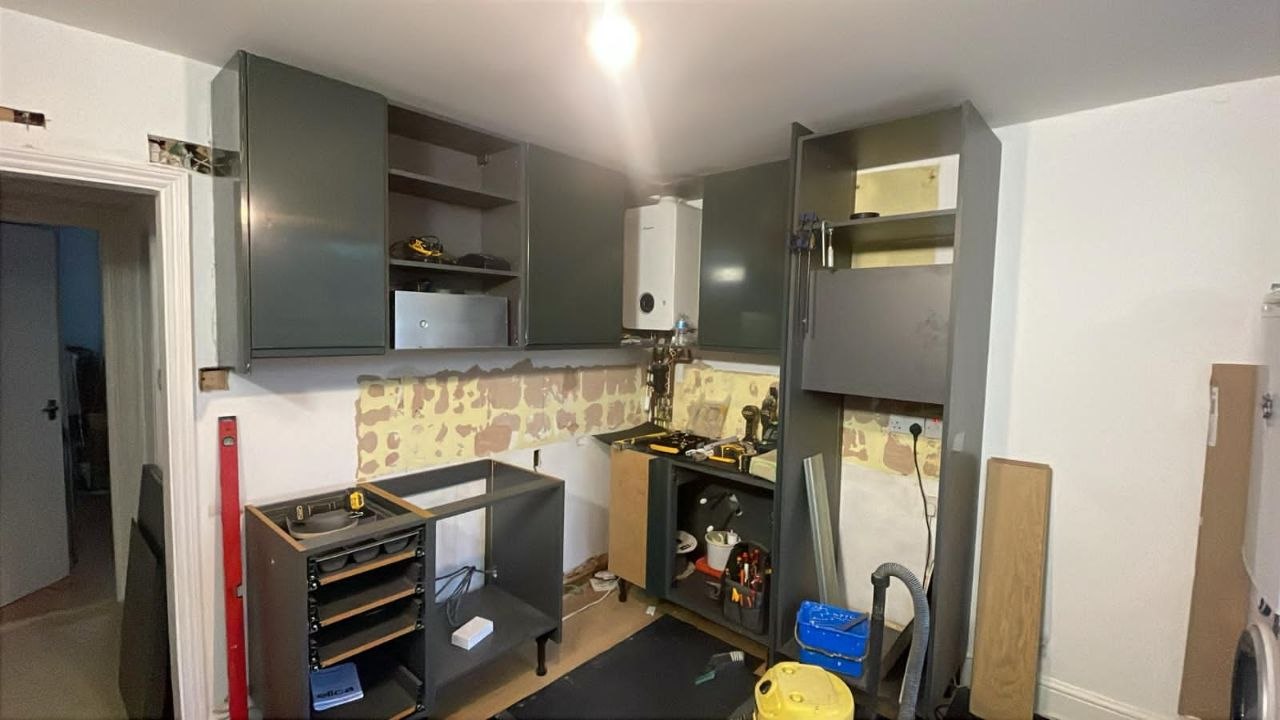 Kitchen during refurbishment with new dark cabinets being fitted and existing boiler retained.