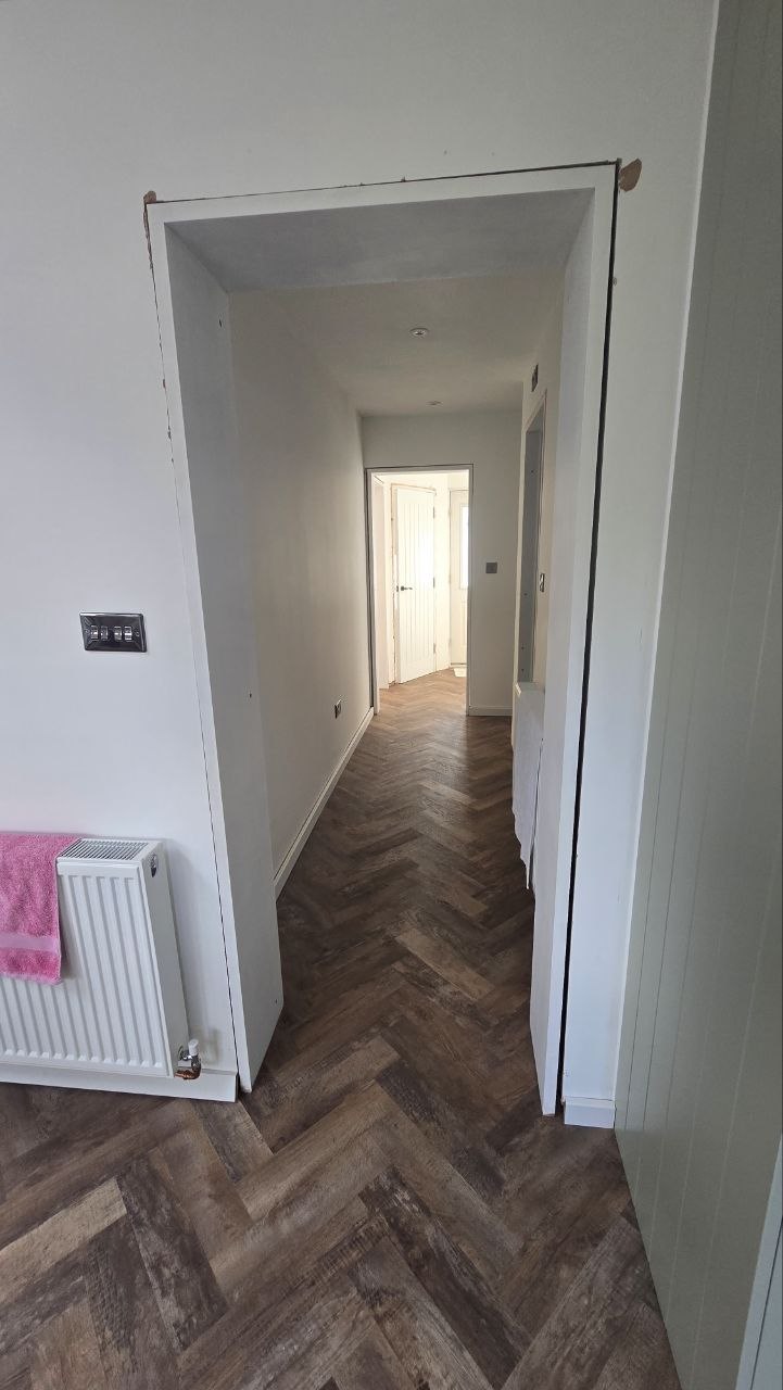 Hallway with herringbone flooring connecting the finished kitchen and adjoining rooms.