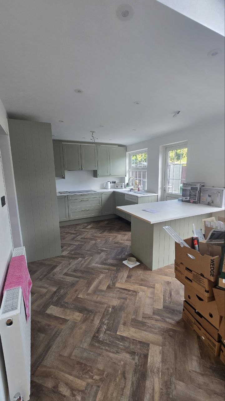 Finished fitted kitchen with pale green cabinets, central island and herringbone flooring.