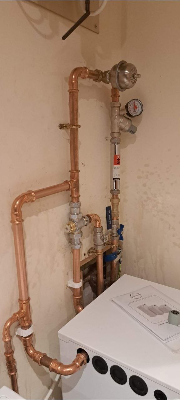 Copper heating pipework, valves and system components connected around a white boiler.