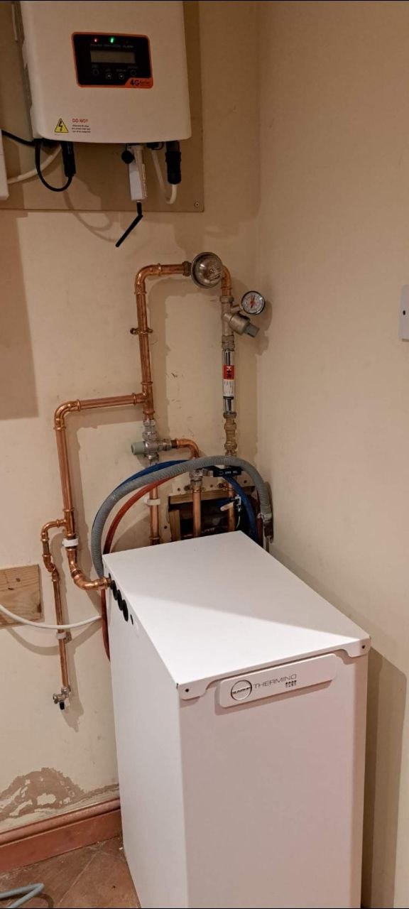 Heating boiler and copper pipework with system components and pressure gauge visible above the boiler.
