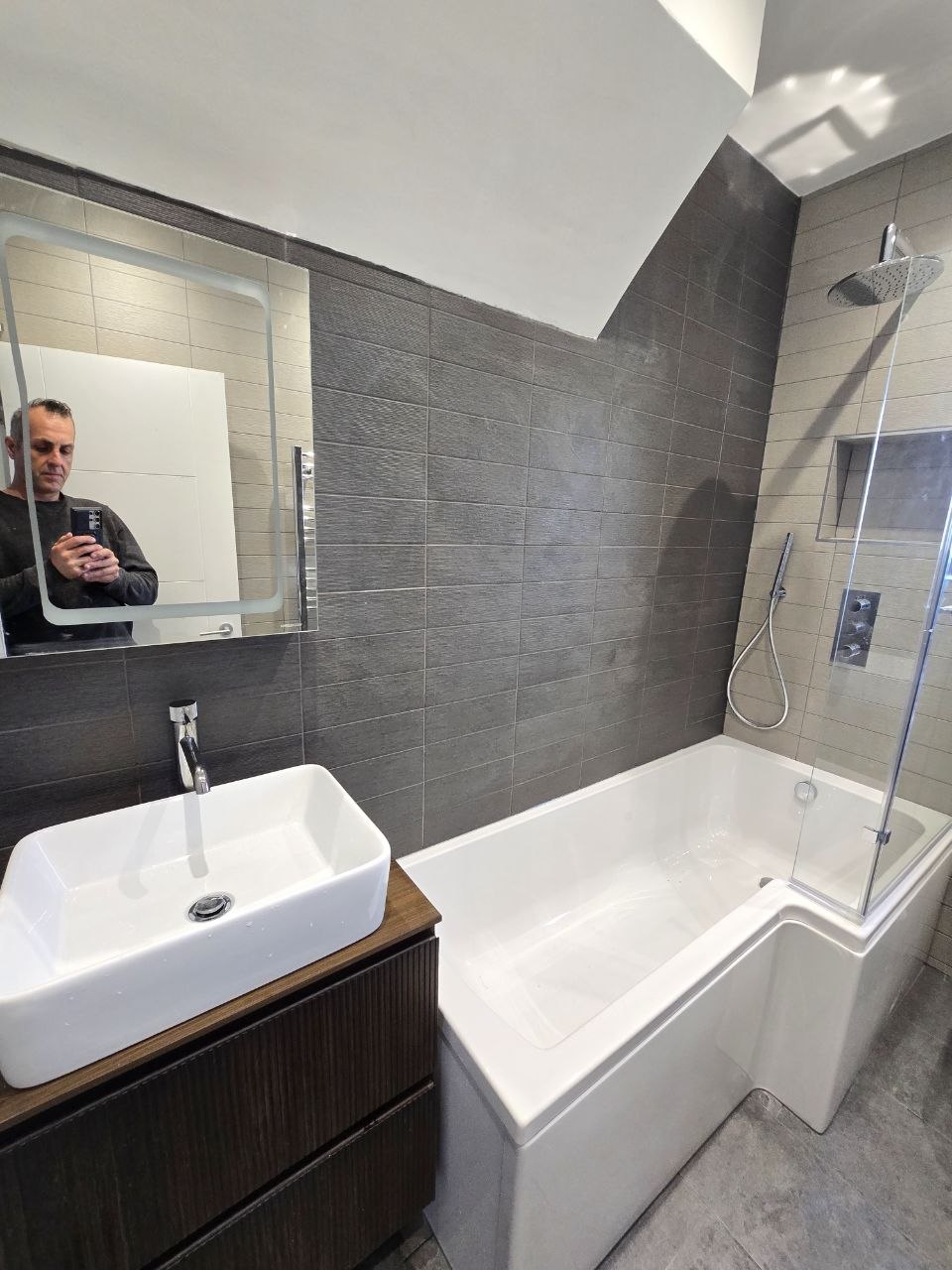 Close view of white basin, vanity unit, bath and grey tiled bathroom walls in North London.