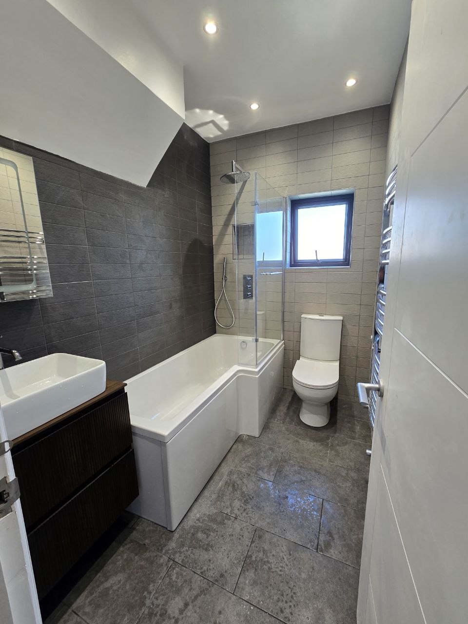 Finished bathroom showing bath, shower, WC, vanity basin and heated towel rail in North London.