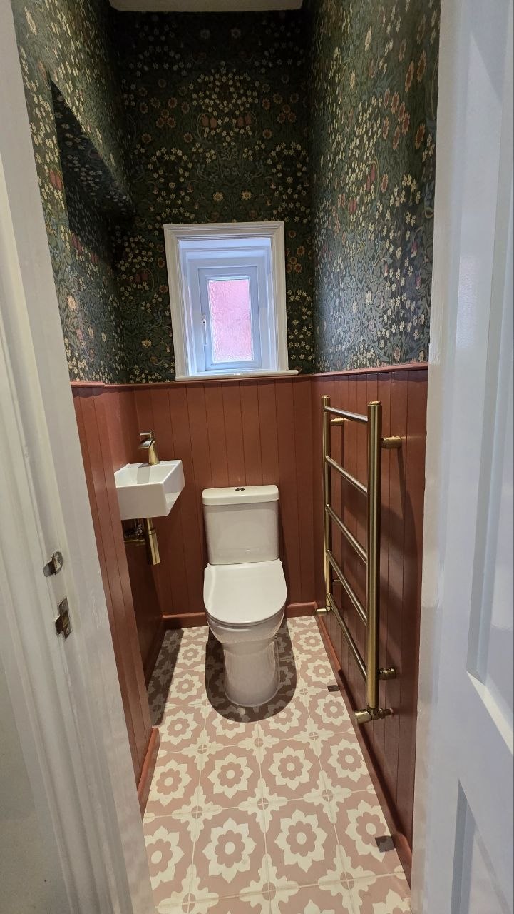 Completed downstairs toilet with WC, wall-mounted basin, floral wallpaper, timber panelling and patterned floor tiles.