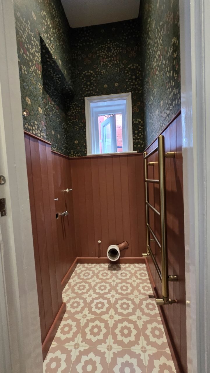 : Finished cloakroom with floral wallpaper, timber panelling, patterned floor tiles and brass-effect heated towel rail.