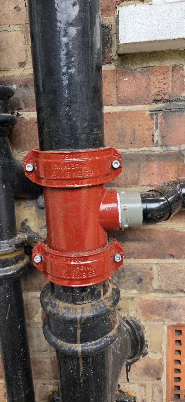 External black soil pipe with red mechanical couplings connected to the drainage system.