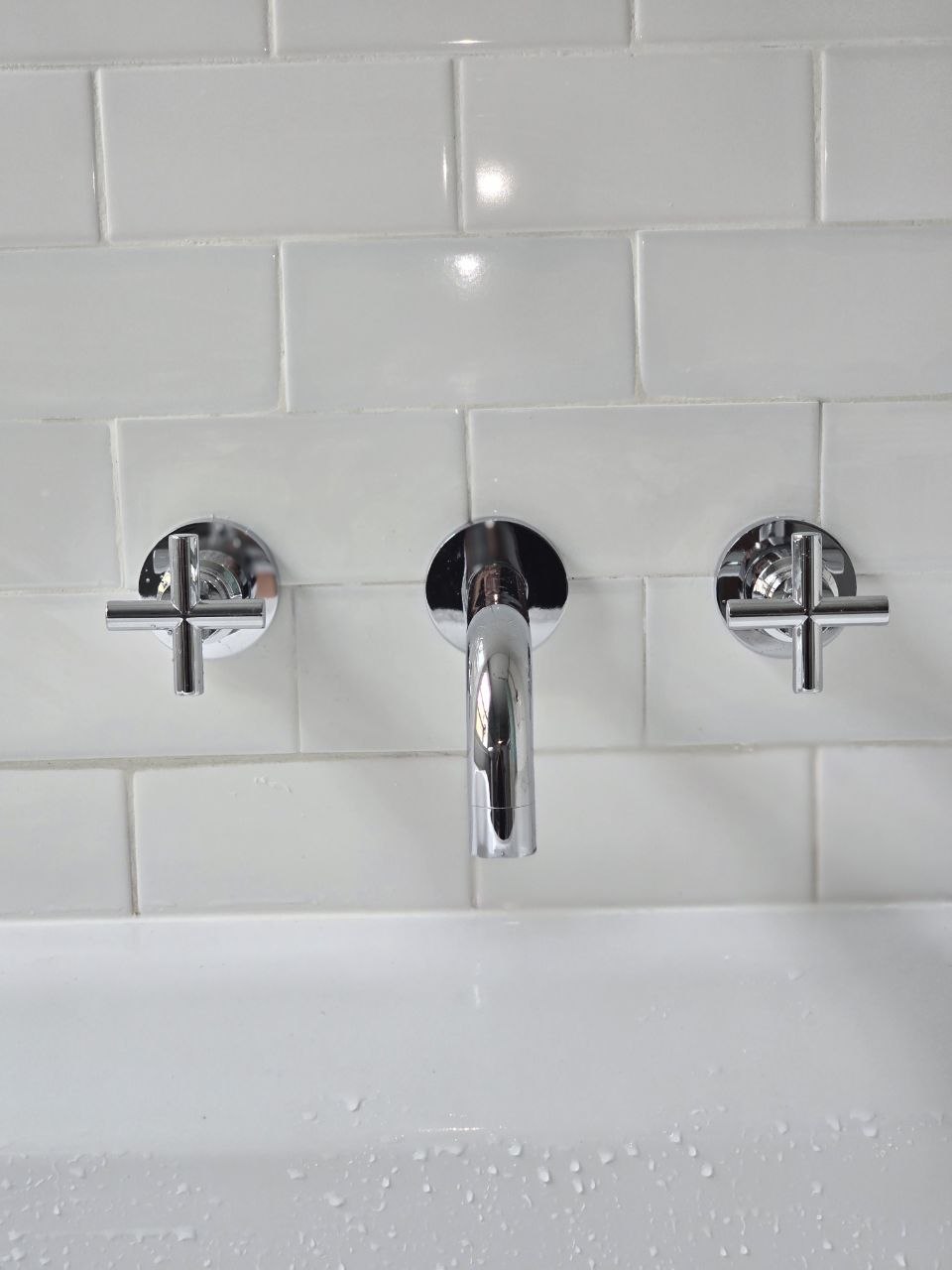 Completed chrome bath tap with two crosshead handles fitted against a white tiled wall.