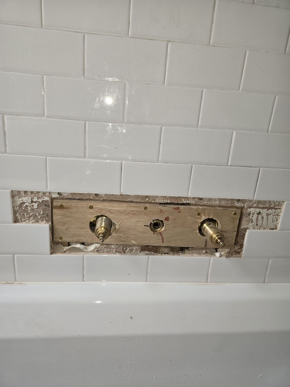 Brass three-hole bath tap fittings mounted on a timber support within the tiled wall.