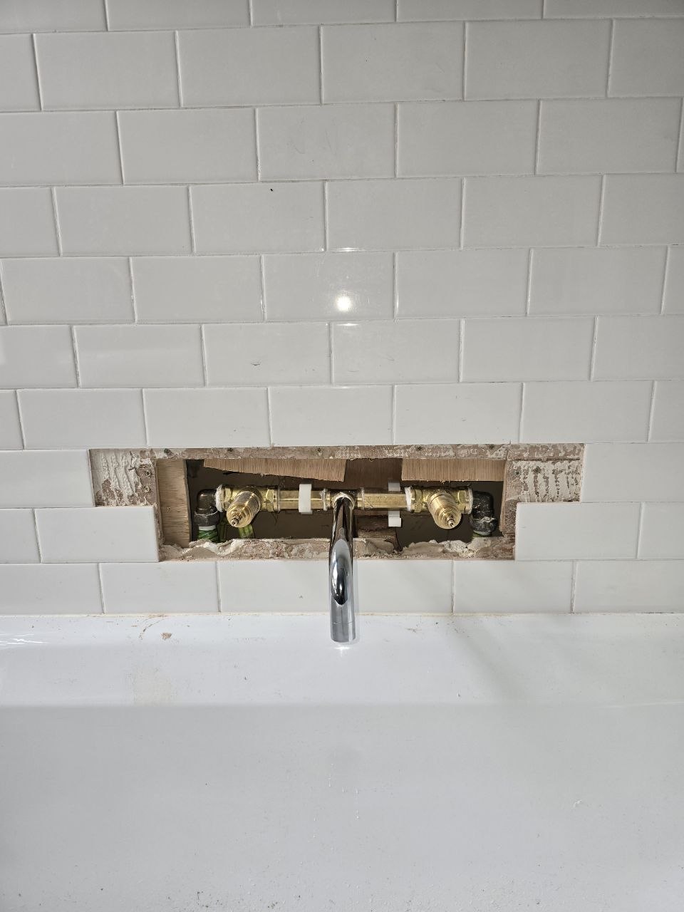 Wall-mounted brass bath tap fittings and chrome spout positioned within the tiled wall.