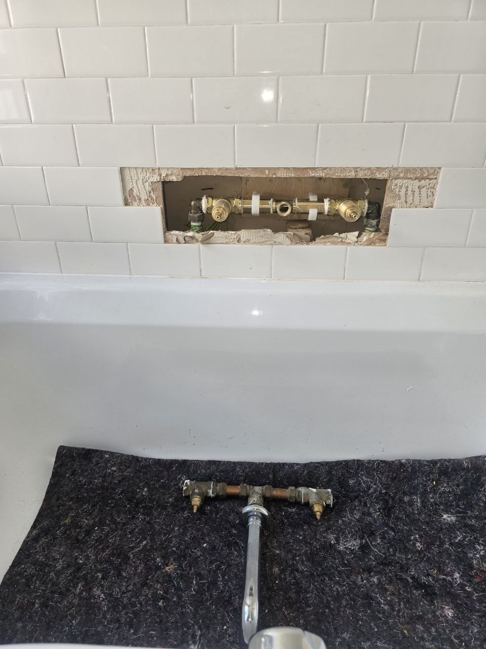 Exposed wall-mounted bath tap valve and pipework during replacement work above the bath.