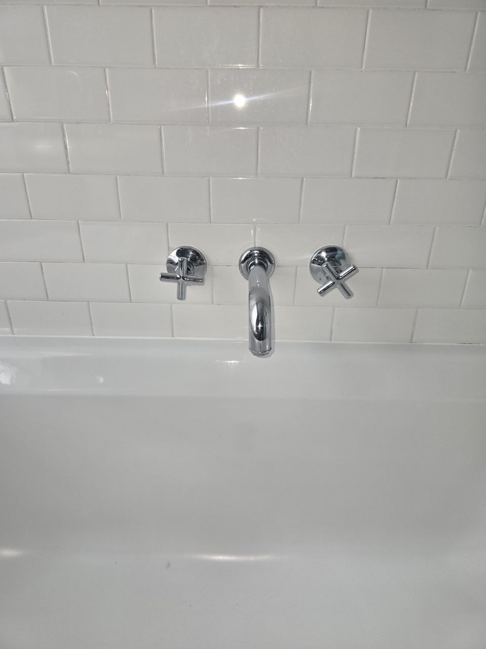 Chrome three-hole wall-mounted bath tap fitted above a white bath with tiled wall.