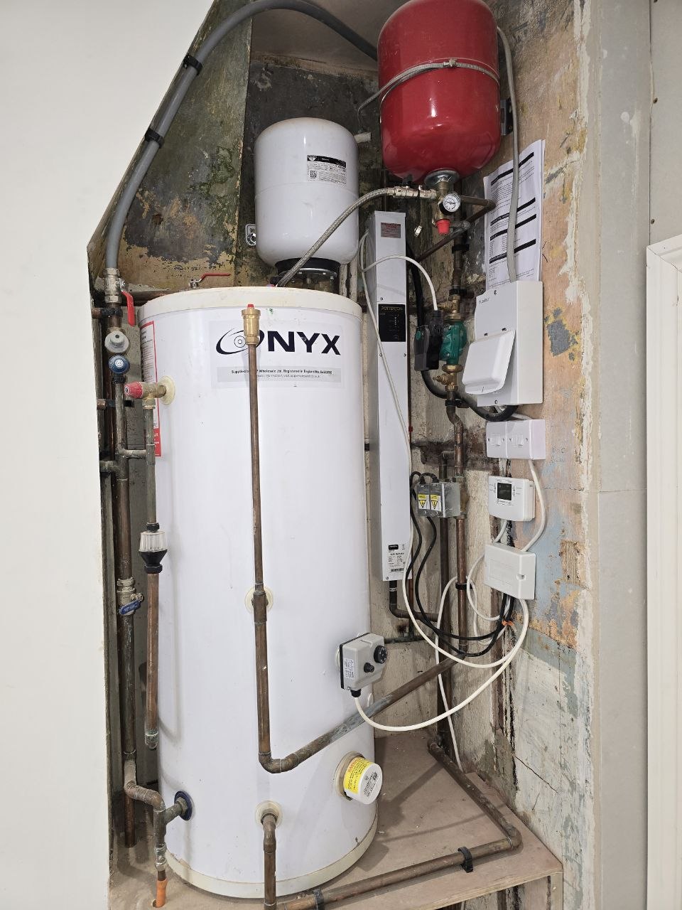 An ONYX hot water cylinder with expansion vessels, copper pipework and heating controls in a plant cupboard.