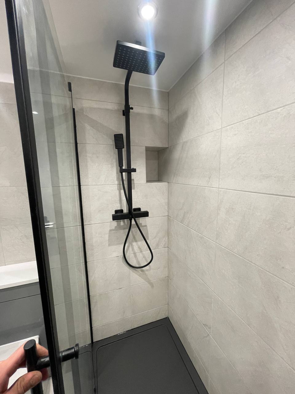Walk-in shower with black shower fittings, glass screen, dark tray and tiled walls.