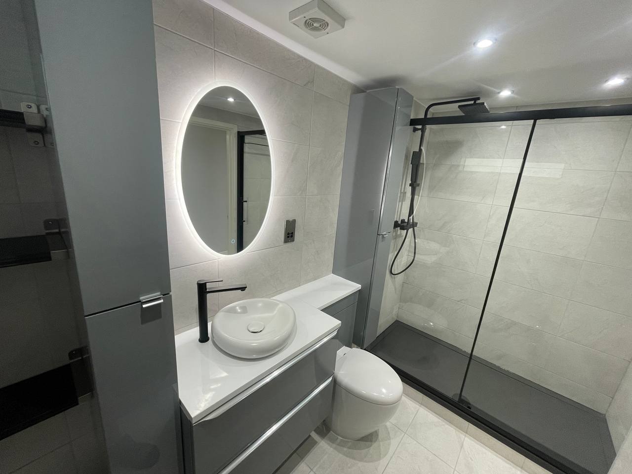 Modern bathroom with walk-in shower, grey vanity unit, countertop basin and black fittings.