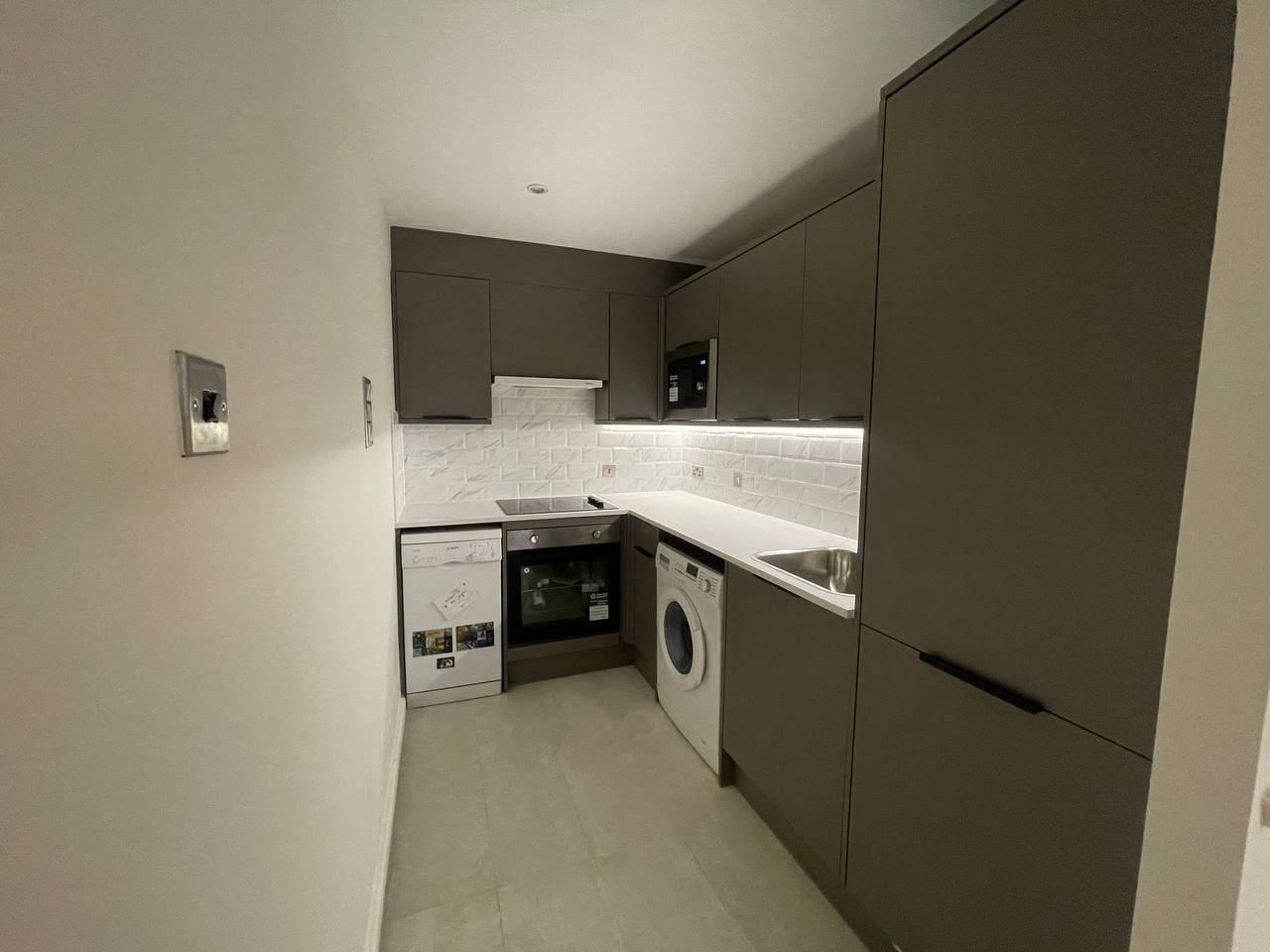 Finished kitchen showing fitted cabinets, worktops, sink, appliances and tiled splashback.