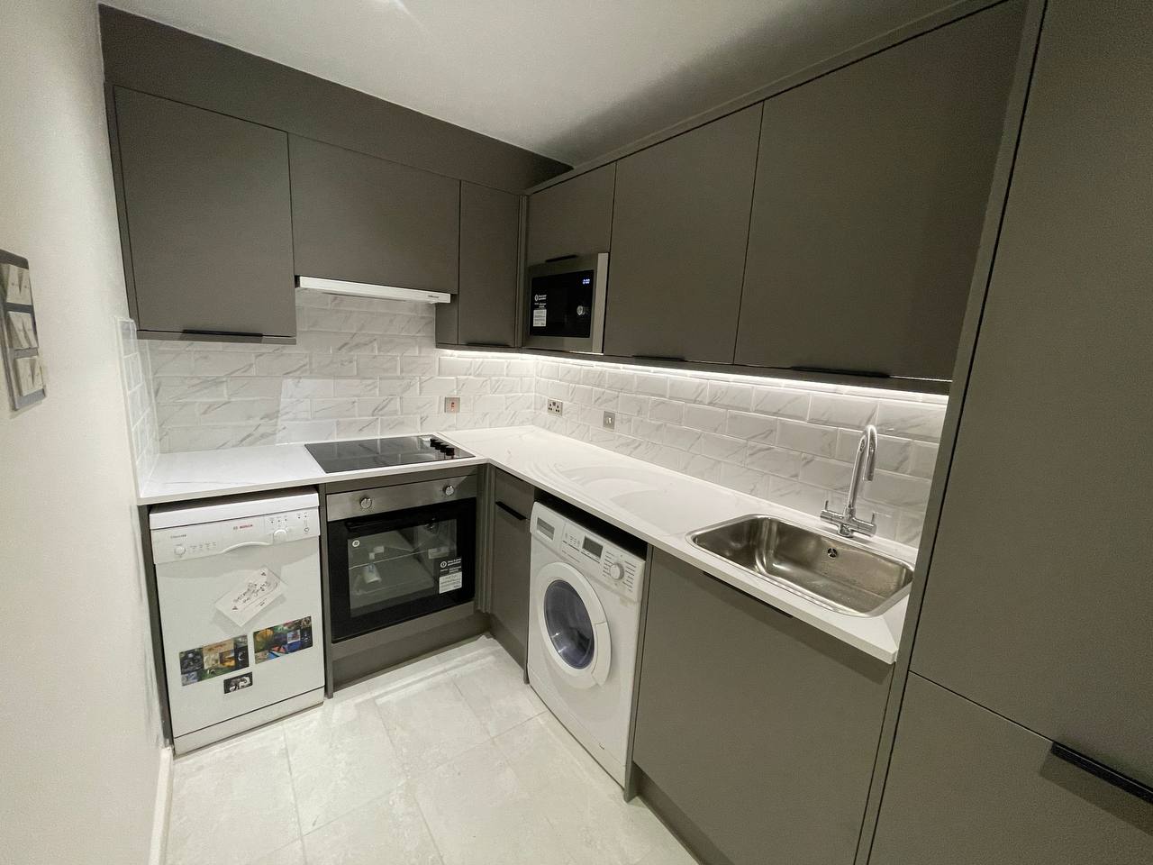 Close view of completed fitted kitchen with white worktops, sink, hob and tiled splashback.