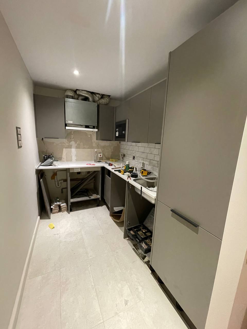 Refurbished kitchen with dark grey cabinets, white worktops, tiled splashback and appliances.